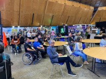 People sitting around tables in the Expo Hall Cafe listening to a presentation