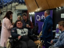 People sitting around tables in the Expo Hall Cafe listening to a presentation