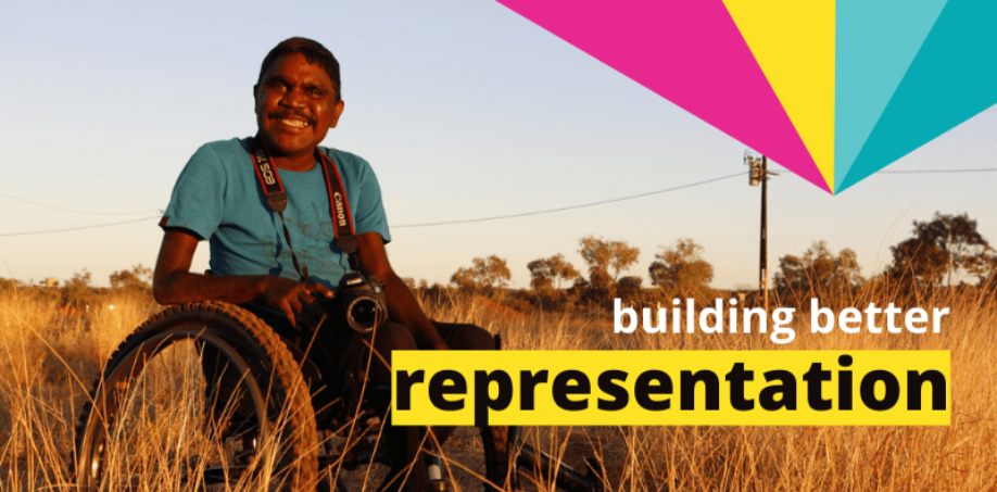 A man with short dark hair is sitting in a wheelchair in a field of long dry grass. The words BUILDING BETTER REPRESENTATION are in the bottom right had corner. A graphic element comprising pink, yellow and blues shapes is in the top right corner.