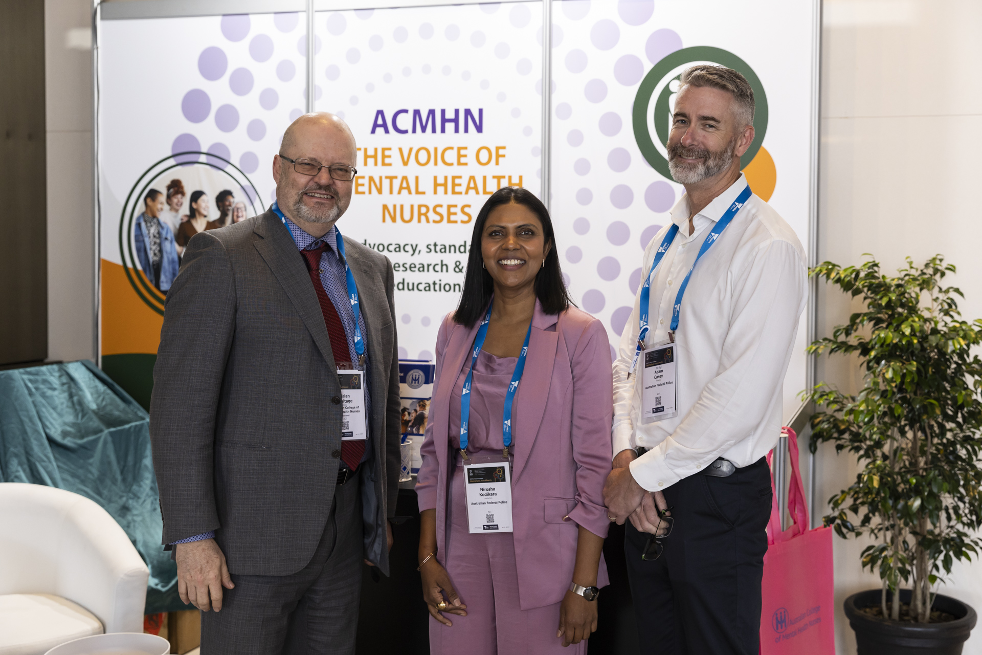 Three delegates smiling in front of the ACMHN exhibition booth.