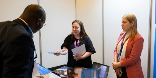 Exhibitor is handing out a flyer to a conference delegate.